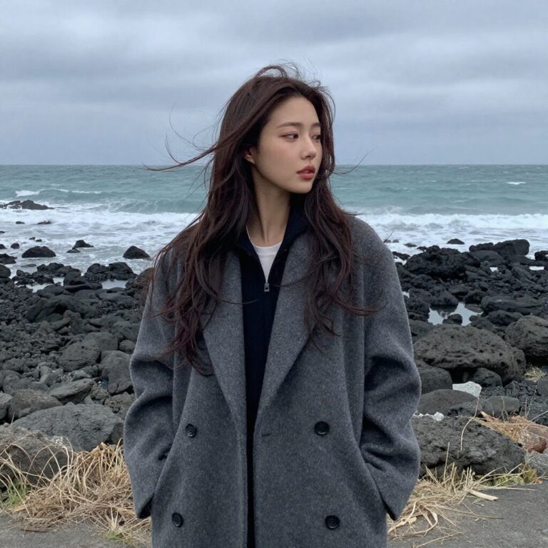 바람이 부는 3월 제주 해변에서 코트를 입고 있는 여성