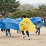 아이들이 밝은 색상의 바람막이를 입고 공원에서 뛰어노는 모습