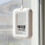 해피홈 에어넷 전기없이 모기 퇴치 효과 방충망에 부착된 해피홈 에어넷 걸이형 모습. 흰색 플라스틱 케이스가 깔끔하게 고정되어 있고, 주변에 창문과 방충망이 보인다.